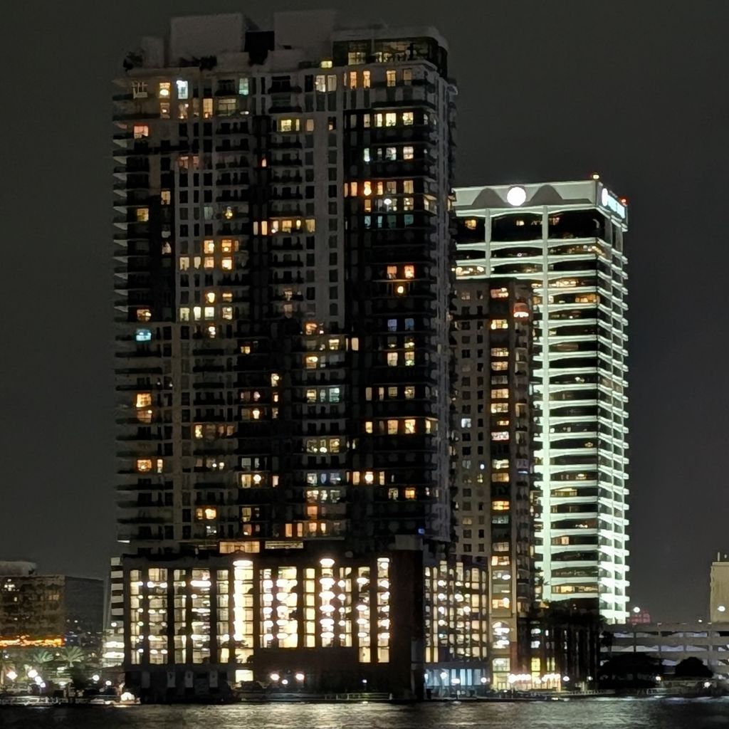Tall waterfront buildings lit up at night from the yacht