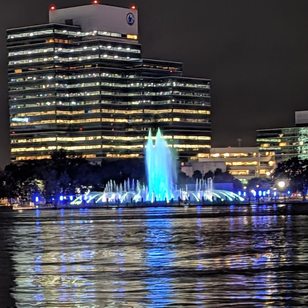 Fountain and waterfront buildings lit at night along the river